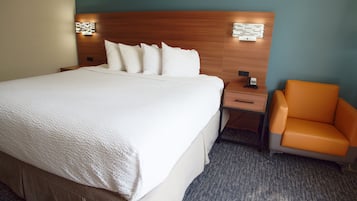 Habitación de hotel con una cama grande, una mesita de noche, una silla y una lámpara fijada a la pared.