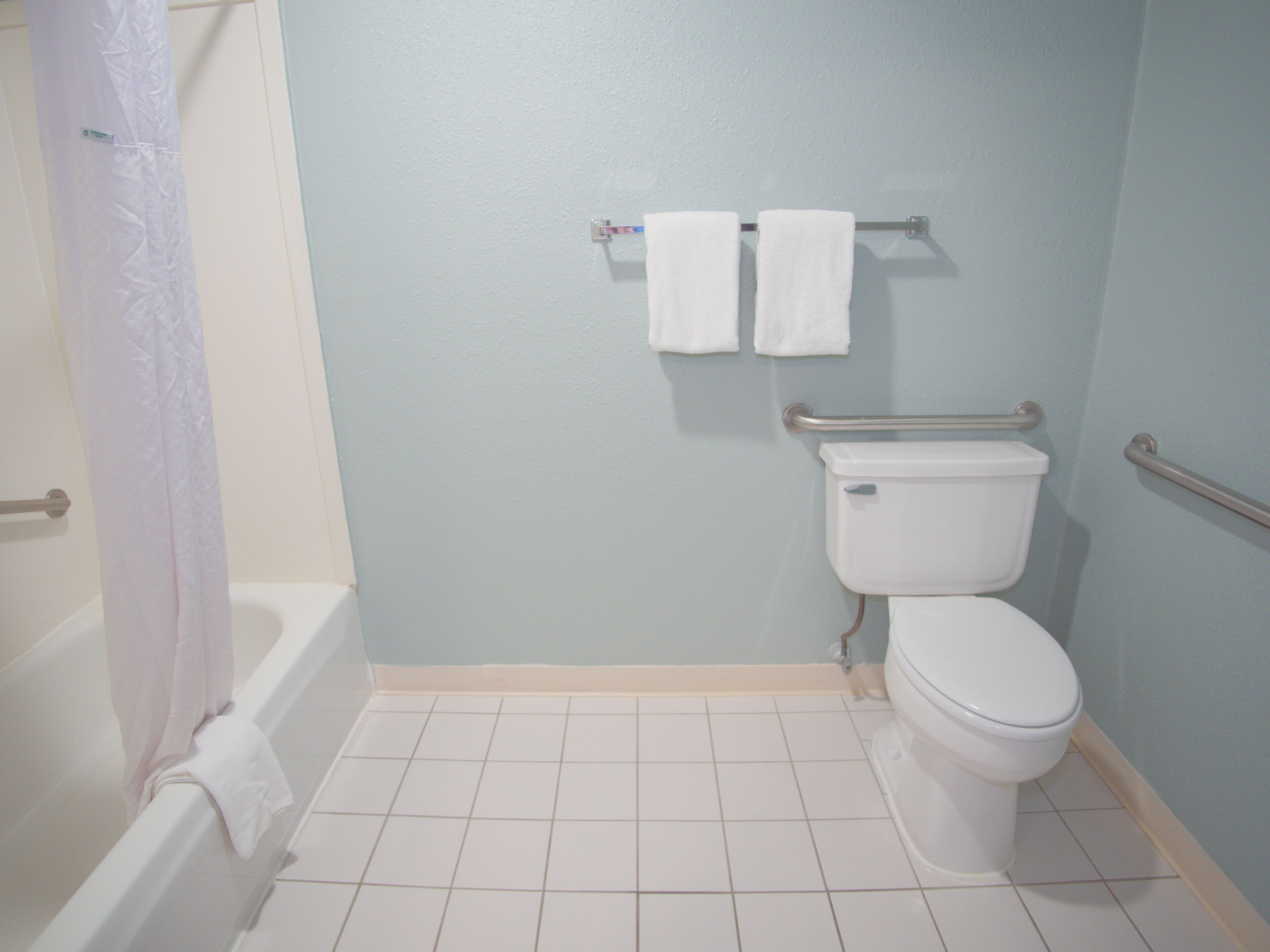 Un baño con bañera, inodoro y barras de apoyo.
