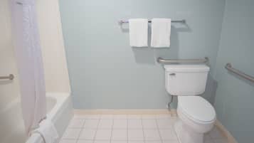 A bathroom with a bathtub, toilet, and handrails.