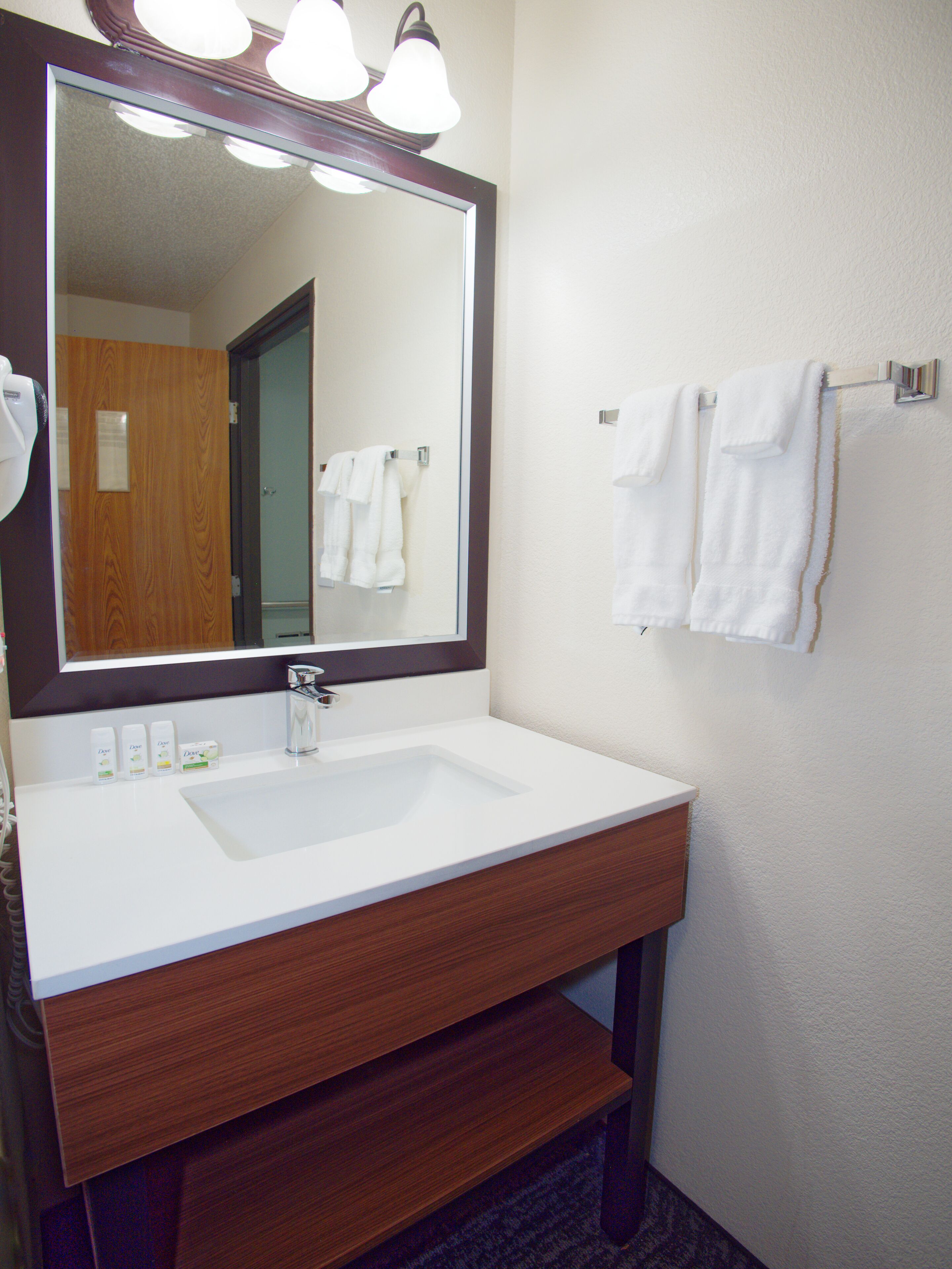 A bathroom with a white sink, wooden vanity, and a large mirror with three lights.
