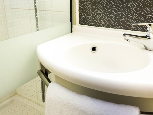 A bathroom with a white sink, a towel hanging on a rack, and a patterned wall. - Ibis Lorient-Caudan (Caudan)