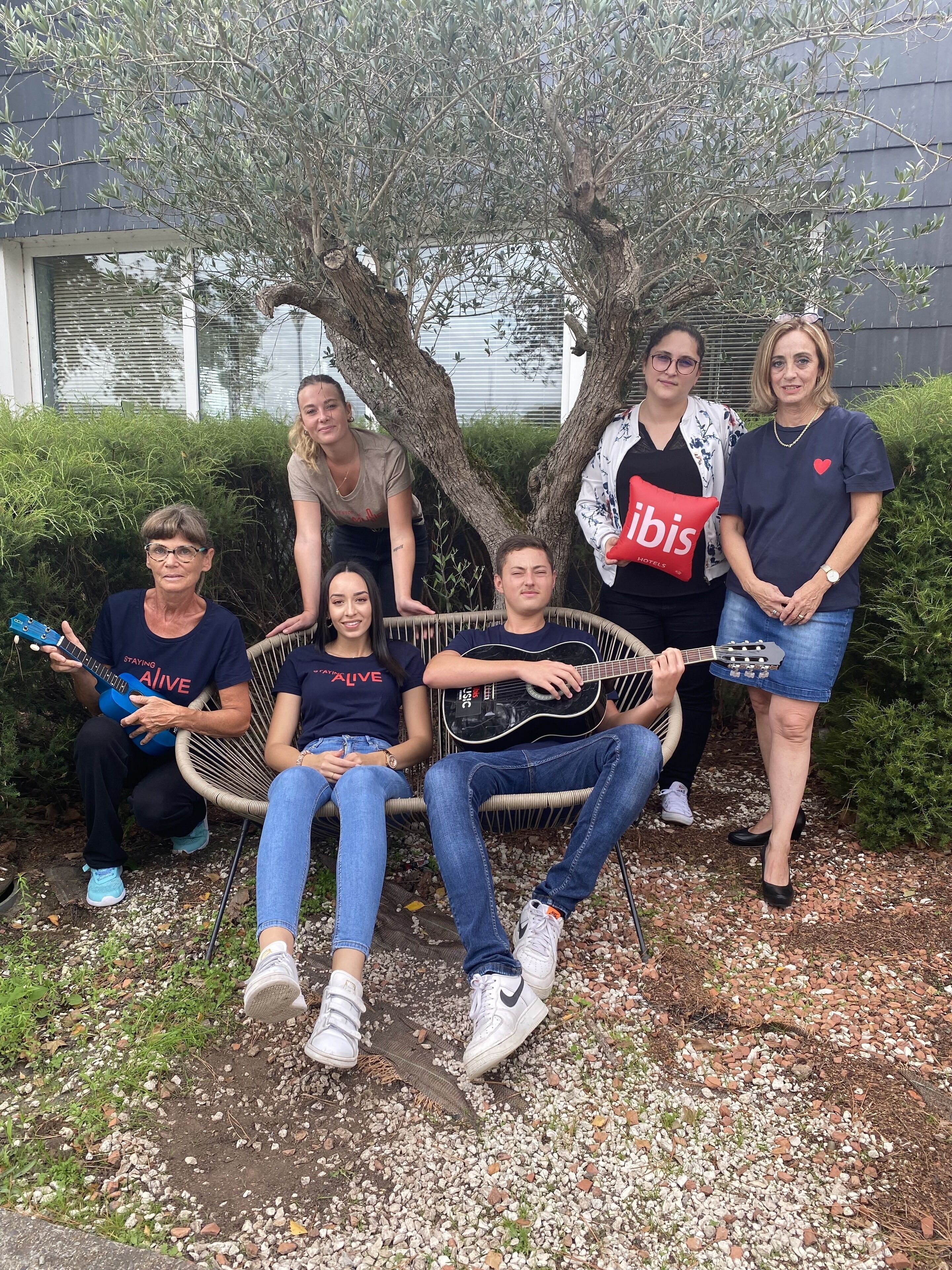 Un groupe de personnes assises et debout à l’extérieur, avec un arbre et un bâtiment en arrière-plan.