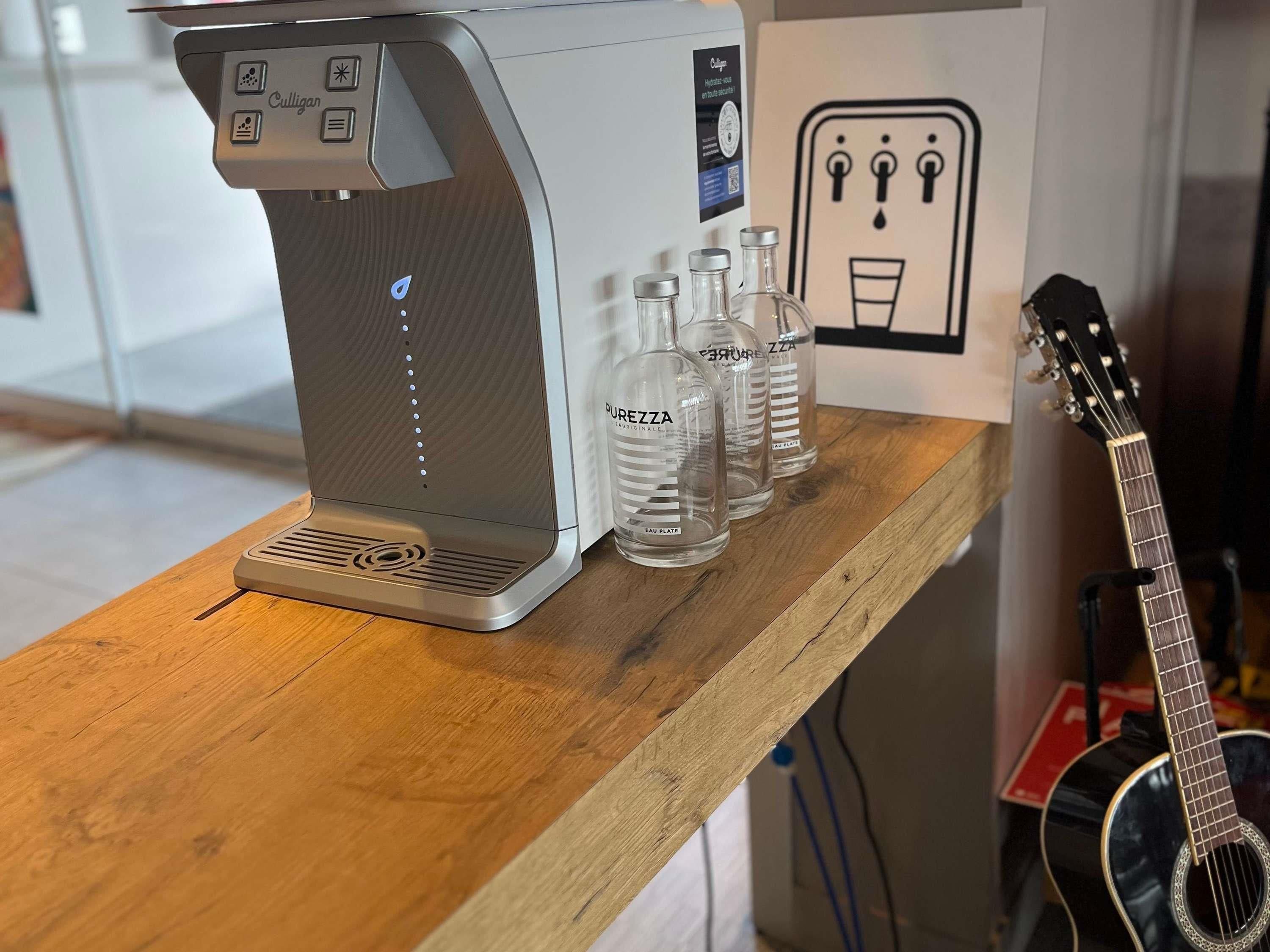 A coffee machine, three water bottles, and a guitar on a wooden table.