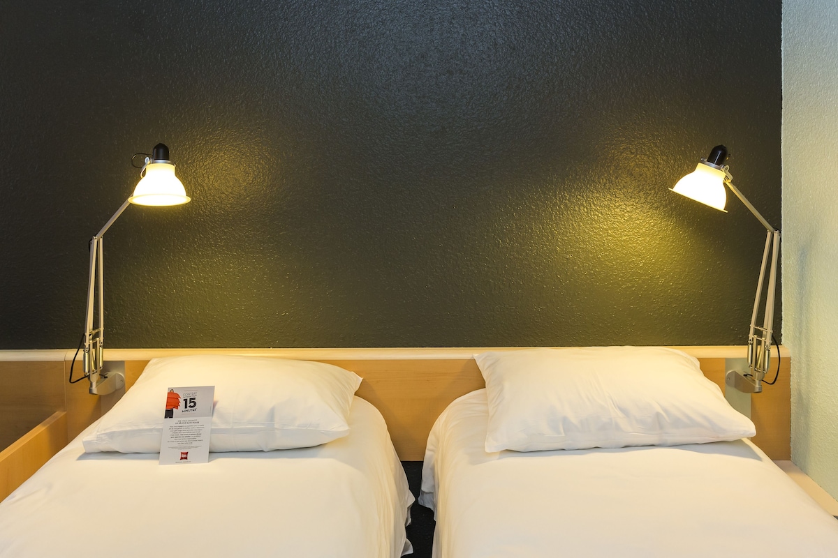 Two single beds with white bedding, a dark textured wall, and two bedside lamps.