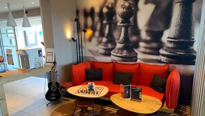 Un interior moderno con un sofá rojo, dos mesas redondas, un tablero de ajedrez, una guitarra y una cafetera.