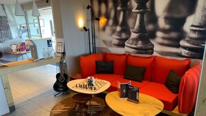 A modern interior with a red sofa, a chess table, and a guitar. - Ibis Lorient-Caudan (Caudan)