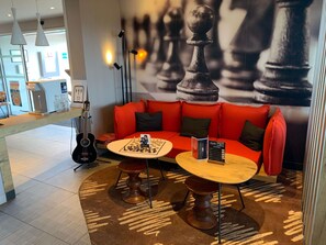 A modern interior with a red sofa, two round tables, a chessboard, a guitar, and a coffee machine.