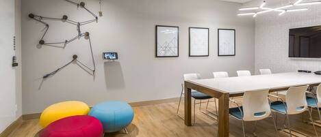 Una sala de reuniones moderna con una mesa blanca, sillas azules y rojas, y arte geométrico en la pared.