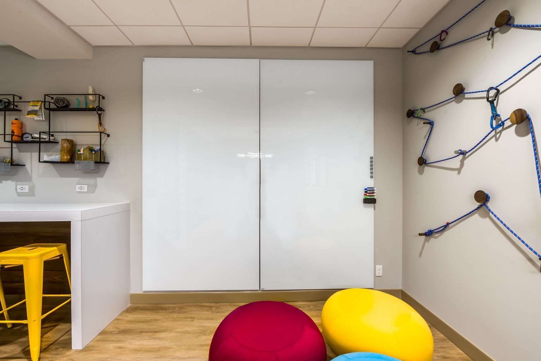 A room with a white wardrobe, a desk with a chair, and a wall with blue exercise equipment.