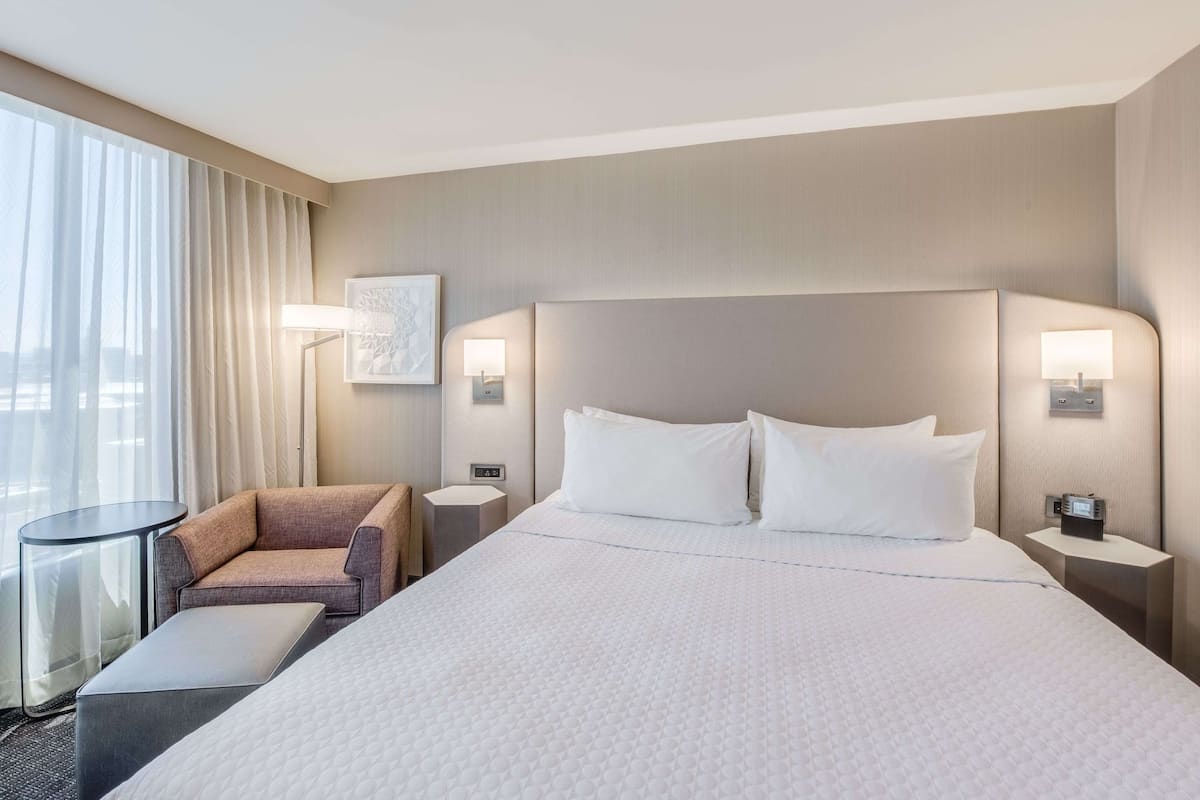 A hotel room with a large bed, two bedside tables with lamps, a chair, and a small table.