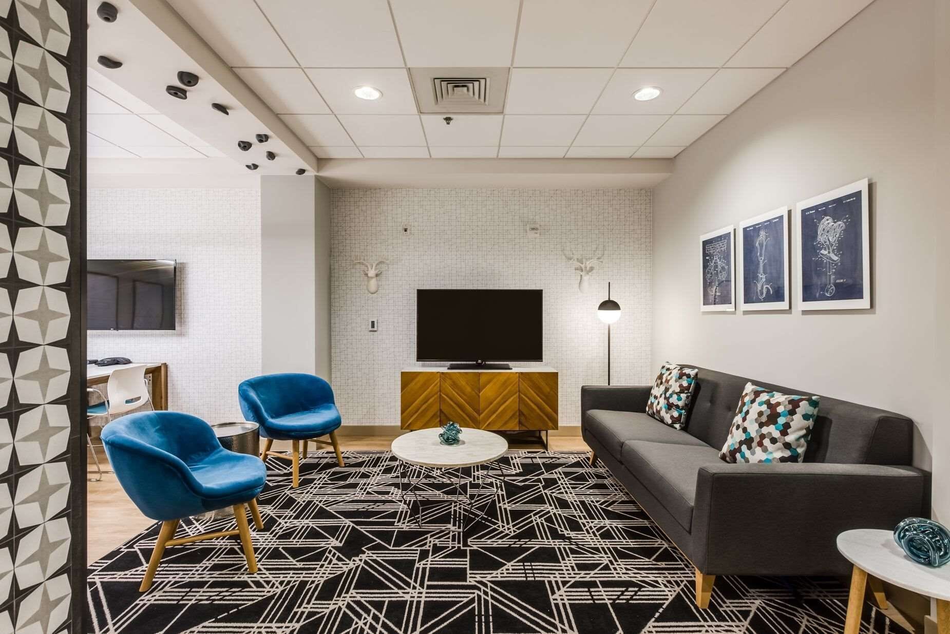 Een moderne woonkamer met een bank, twee blauwe stoelen, een salontafel en een televisie.