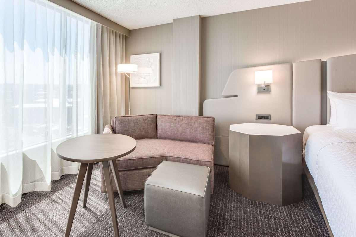 A hotel room with a sofa, a small round table, a bedside table, and a bed.