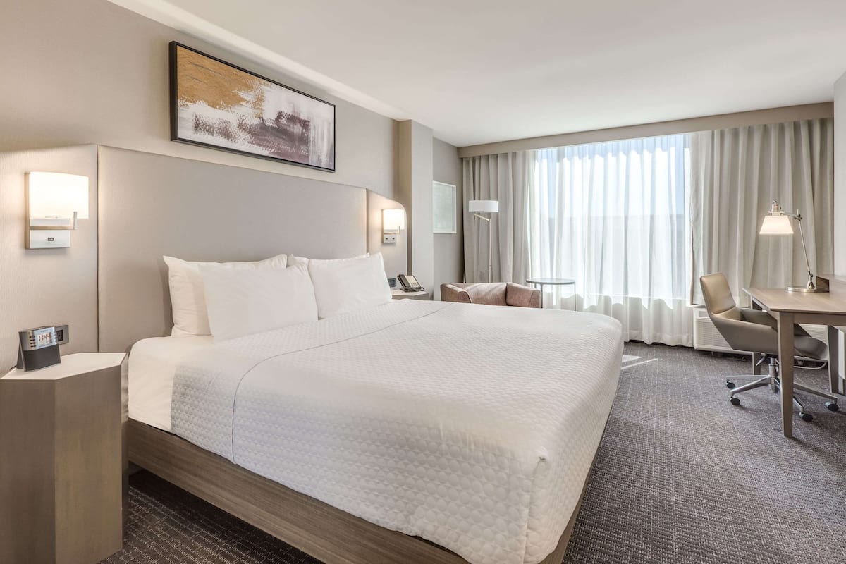 A hotel room with a large bed, a desk, a chair, and a window with curtains.