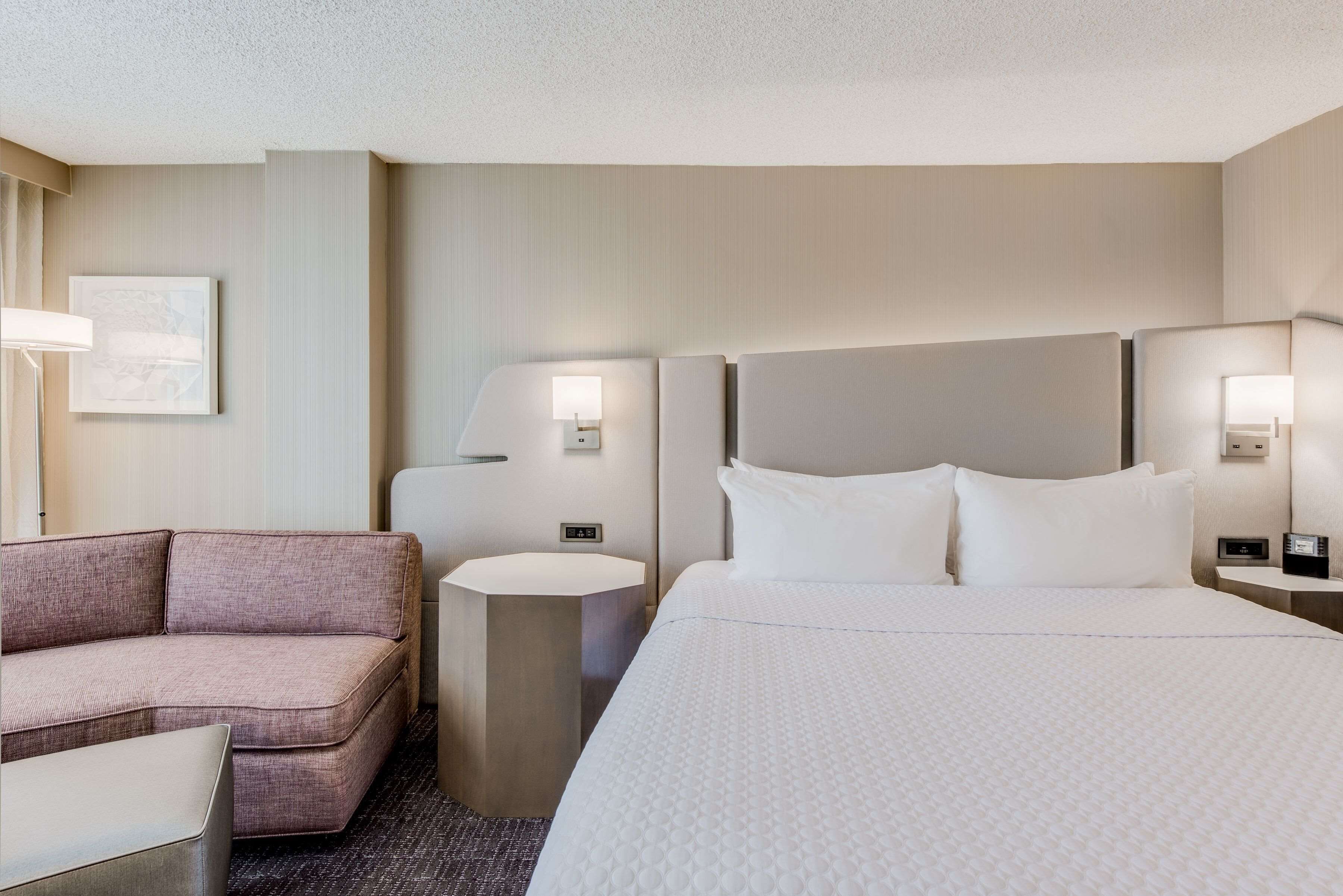A hotel room with a bed, a sofa, a round table, and two wall-mounted lamps.