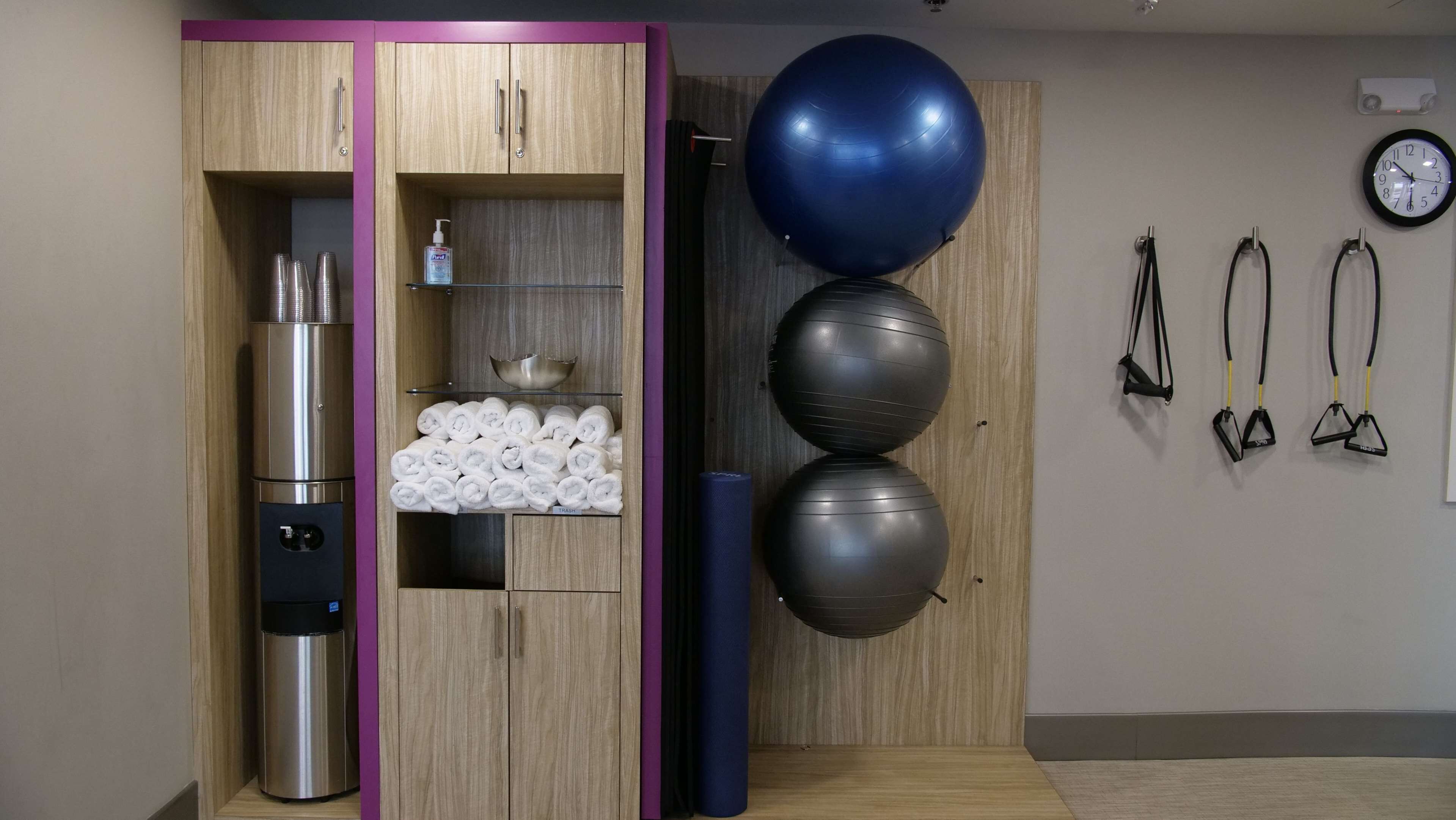 Una habitación con un armario de madera, un electrodoméstico de acero inoxidable, un estante con toallas, una pelota de ejercicio azul y bandas de resistencia.