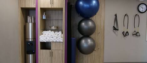 A room with a wooden wardrobe, a stainless steel appliance, a shelf with towels, a blue exercise ball, and resistance bands.
