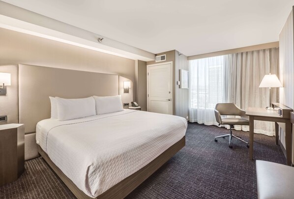 Una habitación de hotel con una cama grande, un escritorio, una silla y una ventana con cortinas.