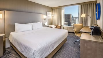 Ein Hotelzimmer mit einem großen Bett, einem Schreibtisch, einem Sessel und Blick auf die Stadt.