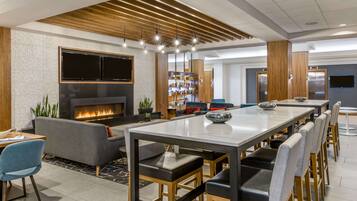 A modern dining area with a long table, chairs, a sofa, and a fireplace.