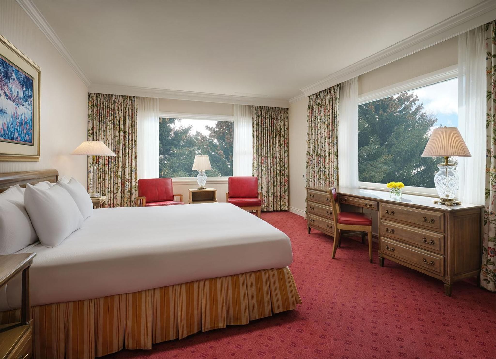 A hotel room with a large bed, a desk, a chair, and a window with a view of trees.