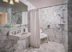 A bathroom with marble walls, a glass shelf with toiletries, a white sink, and a shower area. - Little America Hotel (Little America)