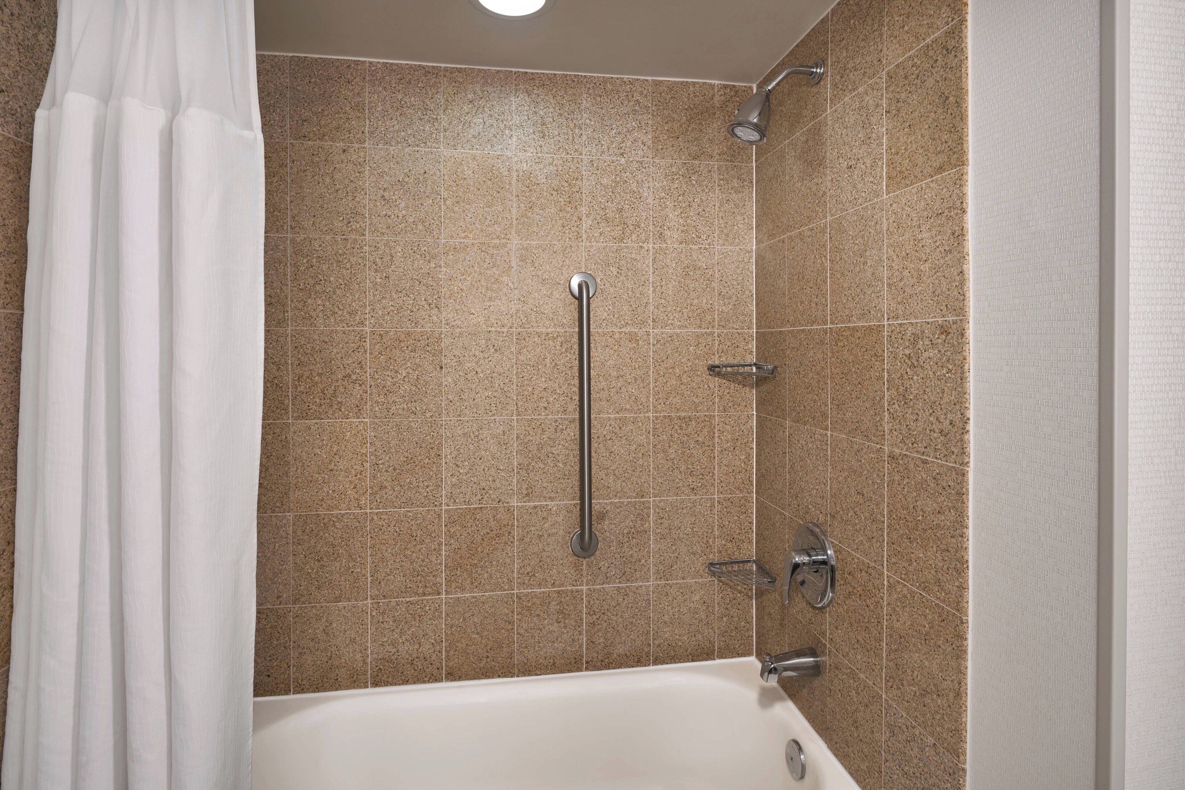 A bathroom with a bathtub, a shower with a grab bar, and tiled walls.
