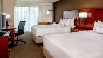 A hotel room with two beds, a desk with a chair, a television, and a window with curtains.