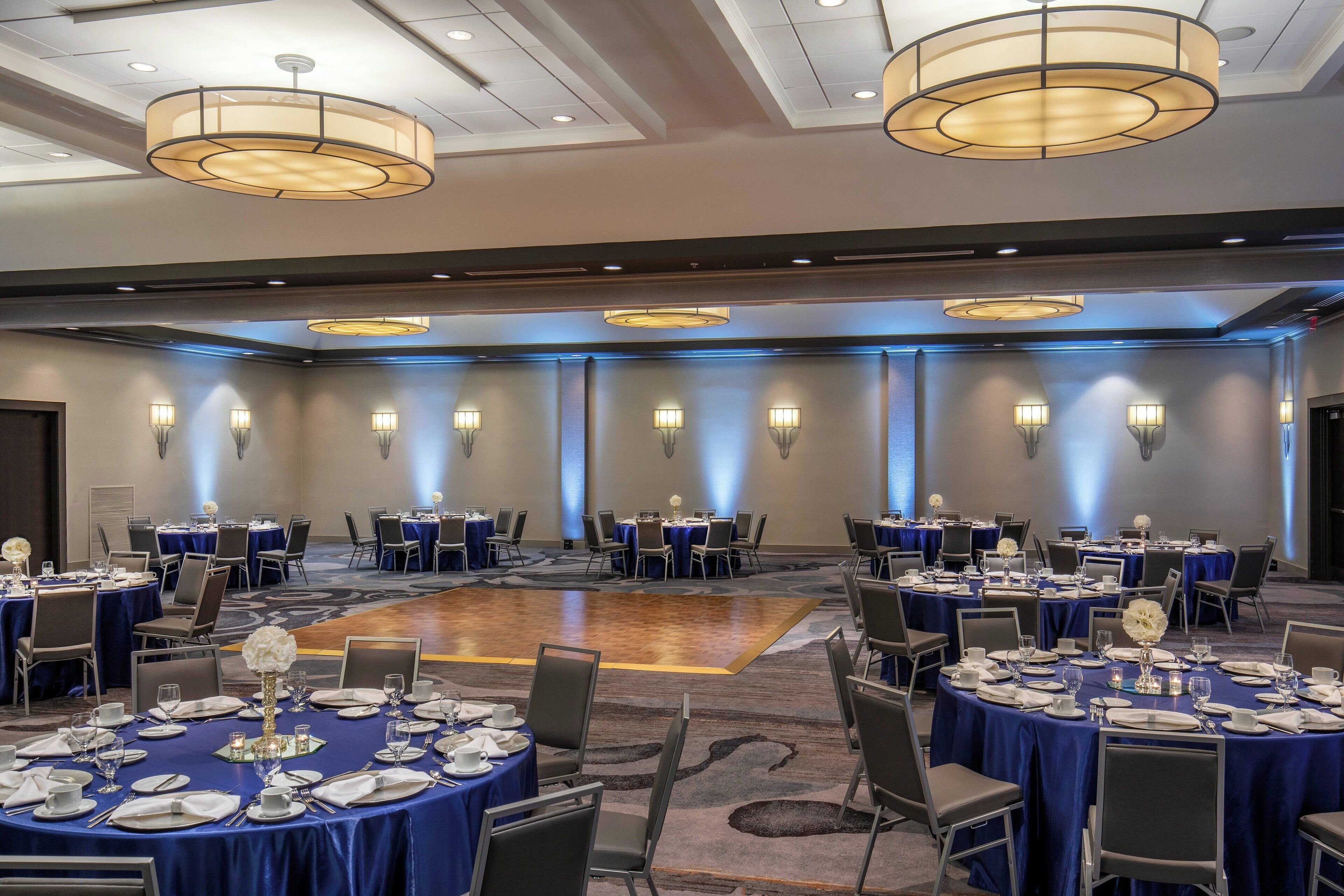 A large conference room with round tables set for dining, equipped with chairs and table settings.