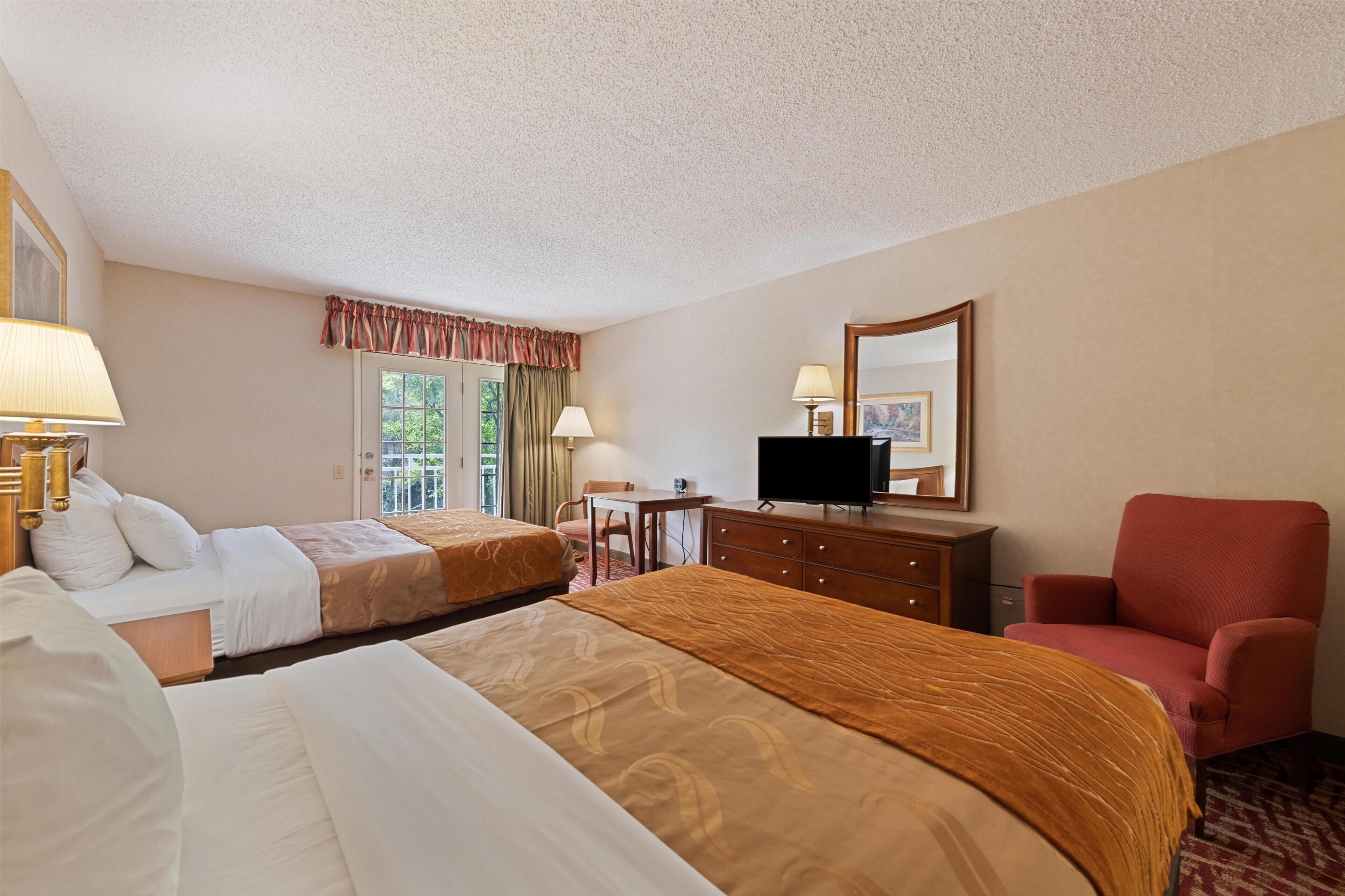 A hotel room with two beds, a television, a desk, a chair, and a window with curtains.