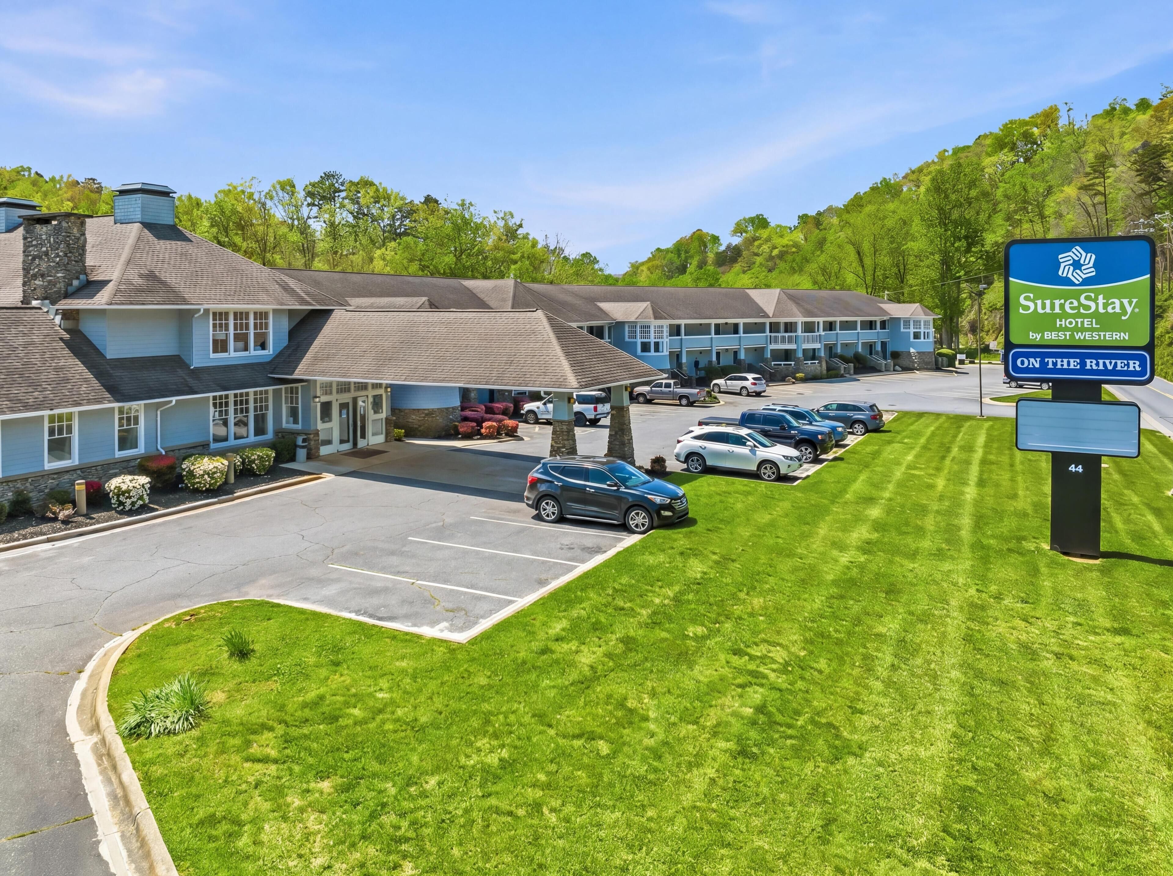 A hotel with a parking lot, a sign for SureStay Hotel by Best Western, and a row of rooms with a view of the river.