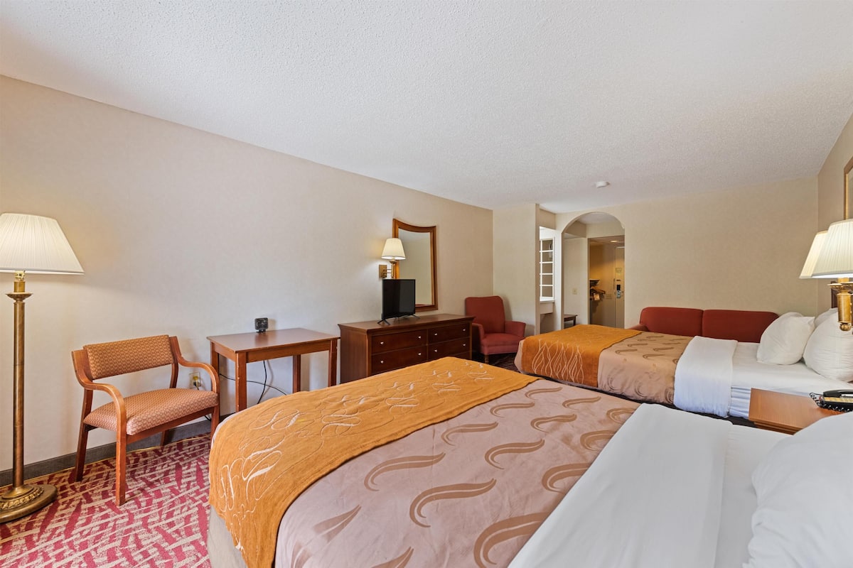 Quarto de hotel com duas camas, uma escrivaninha, uma cadeira, um armário e uma televisão.