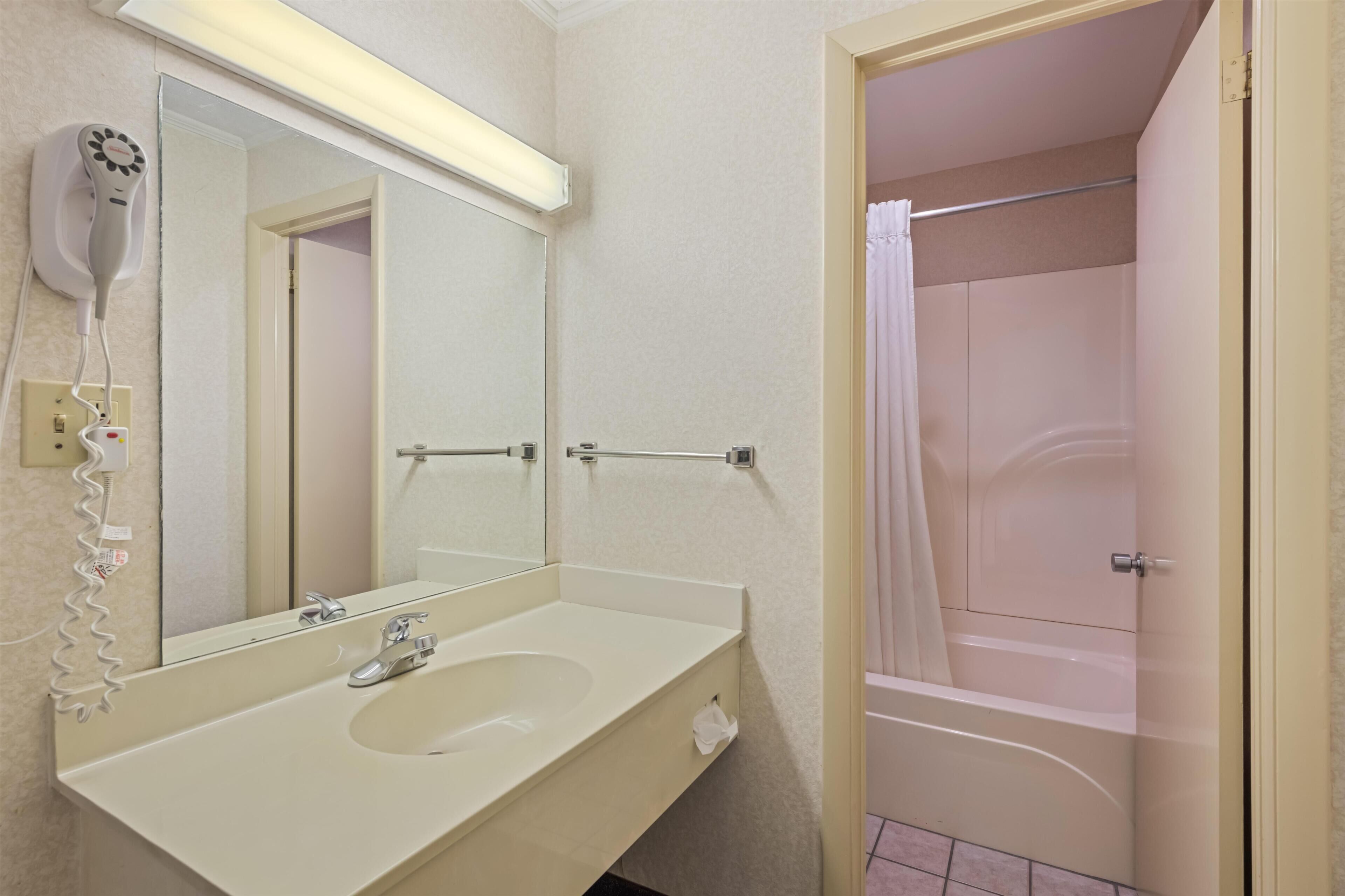 A bathroom with a sink, mirror, hair dryer, and a shower area.
