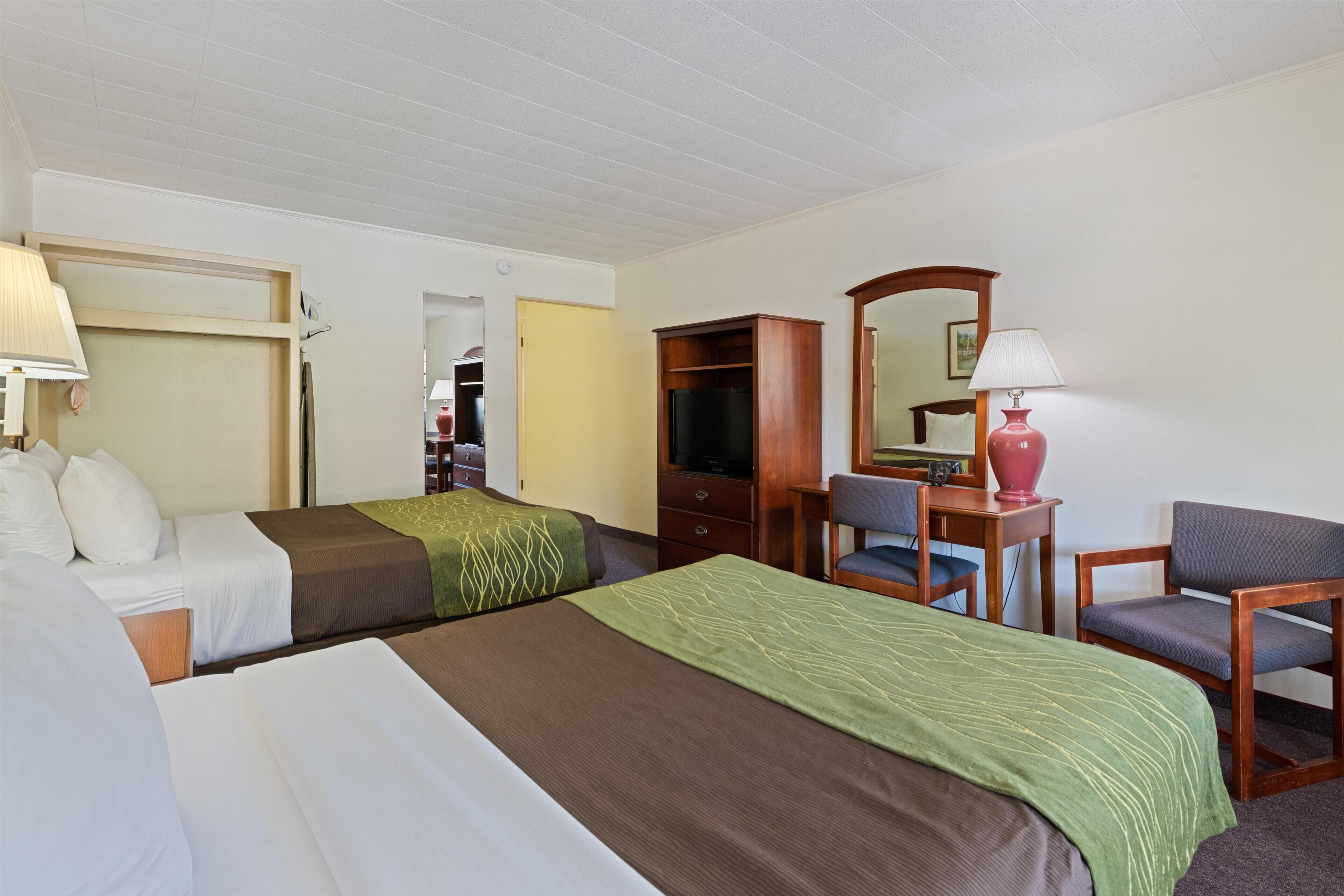 Une chambre d’hôtel avec deux lits, un bureau, une chaise, une télévision et un miroir.