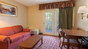 A room with a sofa, a table, a lamp, a painting, and a window with curtains. - SureStay by Best Western Cherokee on the River (Cherokee)