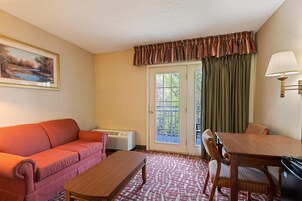 Una habitación con sofá, mesa, lámpara, un cuadro y una ventana con cortinas.