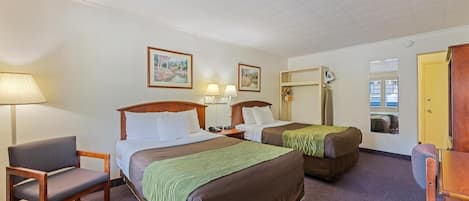 A hotel room with two beds, a chair, a desk, a lamp, and two framed pictures on the wall.