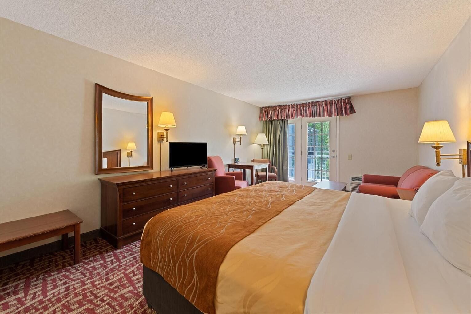A hotel room with a large bed, a desk, a chair, a television, and a window with curtains.