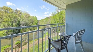 A balcony with a view of a river and forest, two chairs, and a table. - SureStay by Best Western Cherokee on the River (Cherokee)