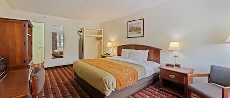 A hotel room with a bed, a desk, a chair, a nightstand, and a lamp.