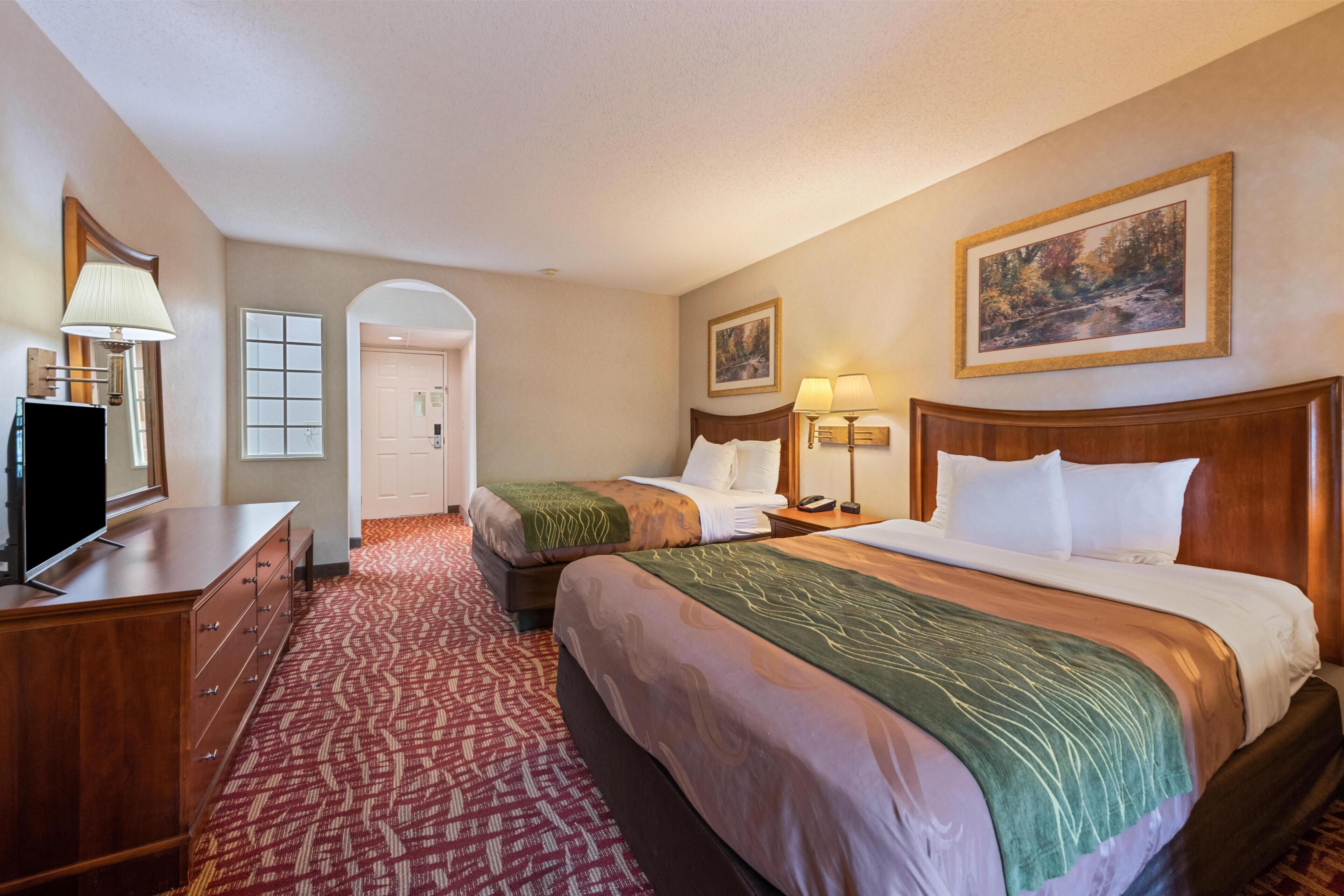 A hotel room with two beds, a dresser, a TV, and a painting on the wall.