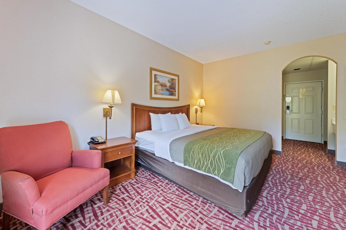 Quarto de hotel com cama, escrivaninha, uma cadeira e duas luminárias fixadas na parede.