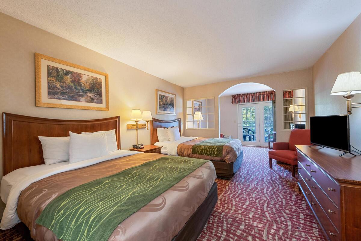 Quarto de hotel com duas camas, televisão, escrivaninha e vista para o exterior.