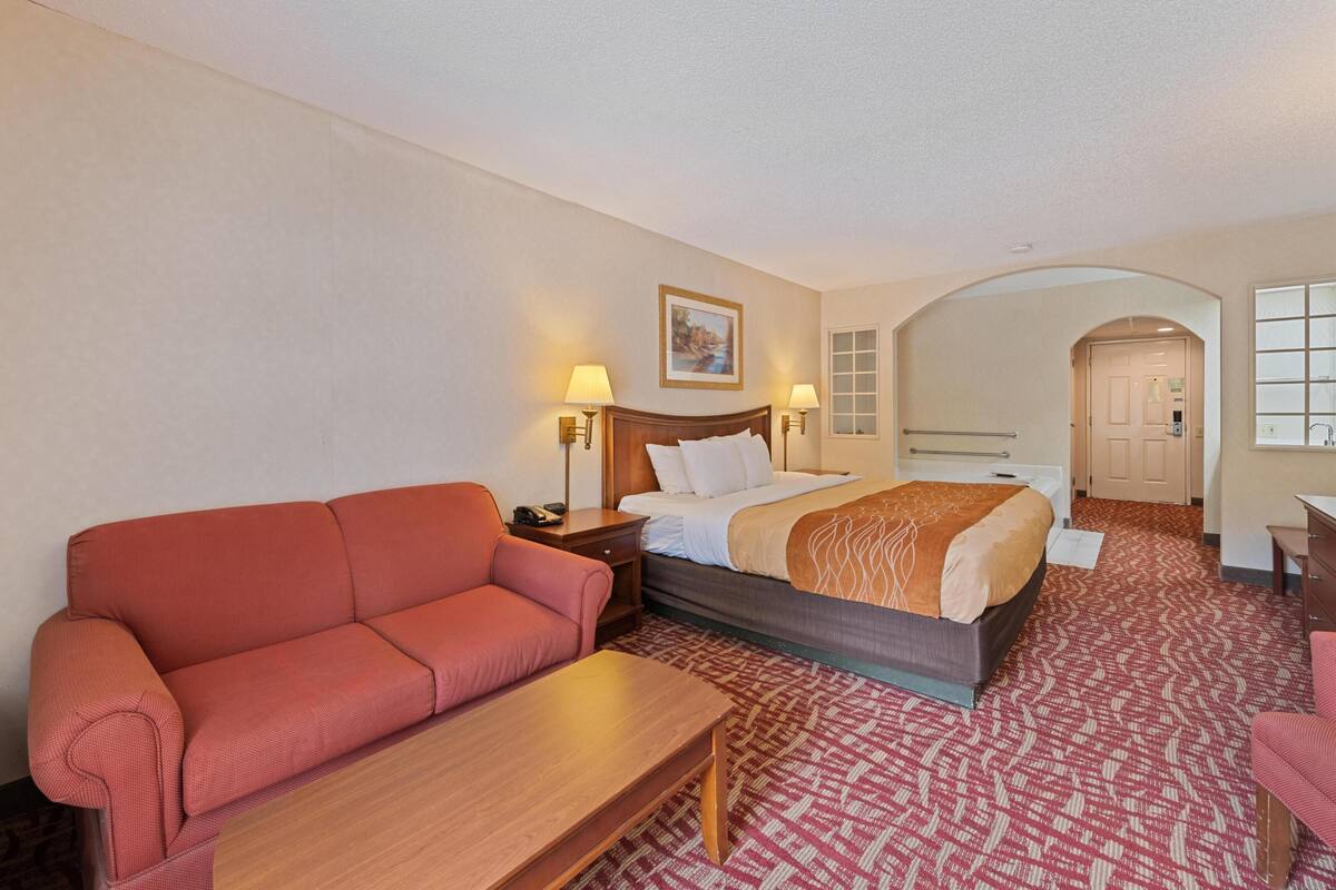 Quarto de hotel com uma cama, um sofá vermelho, uma mesa de madeira e um tapete estampado.
