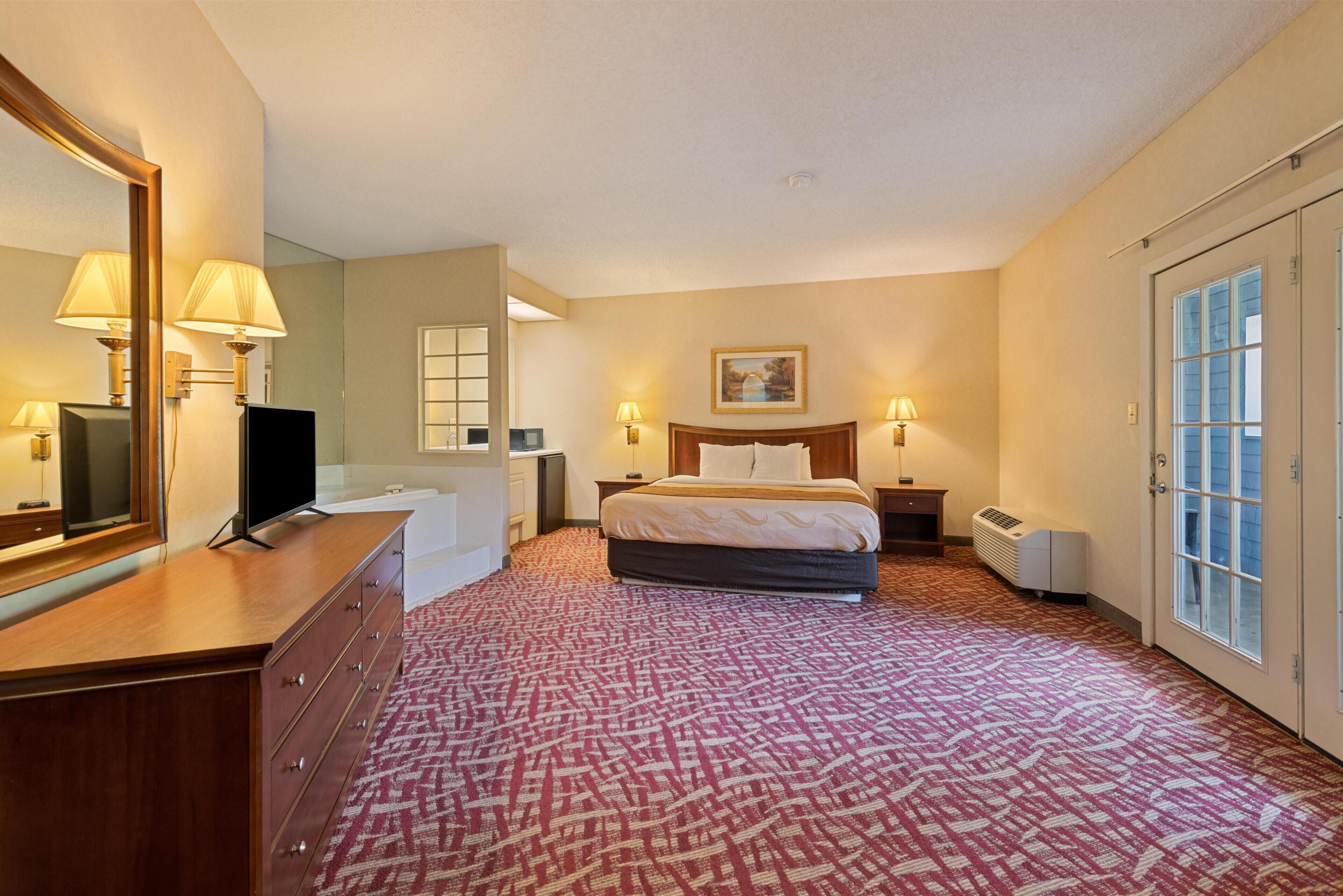 Ein Hotelzimmer mit einem Bett, einem Schminktisch, einem Fernseher, einem Schreibtisch und einem großen Spiegel.