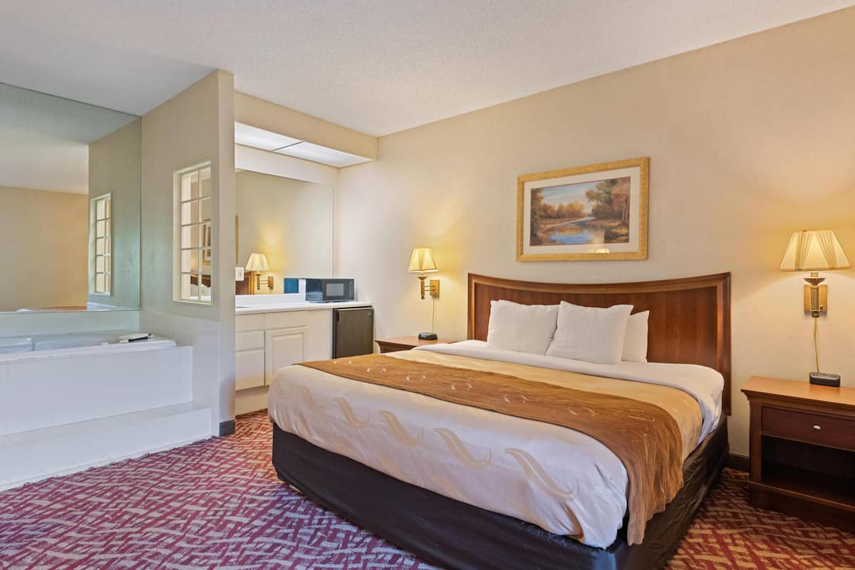Quarto de hotel com cama, escrivaninha, espelho, quadro e banheiro.