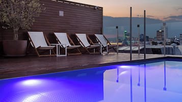 A rooftop pool area with lounge chairs and a potted tree.
