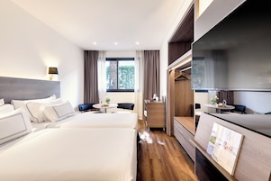 Ein Hotelzimmer mit zwei Betten, einem Fernseher, einem Schreibtisch und einem kleinen Tisch mit einer Pflanze.
