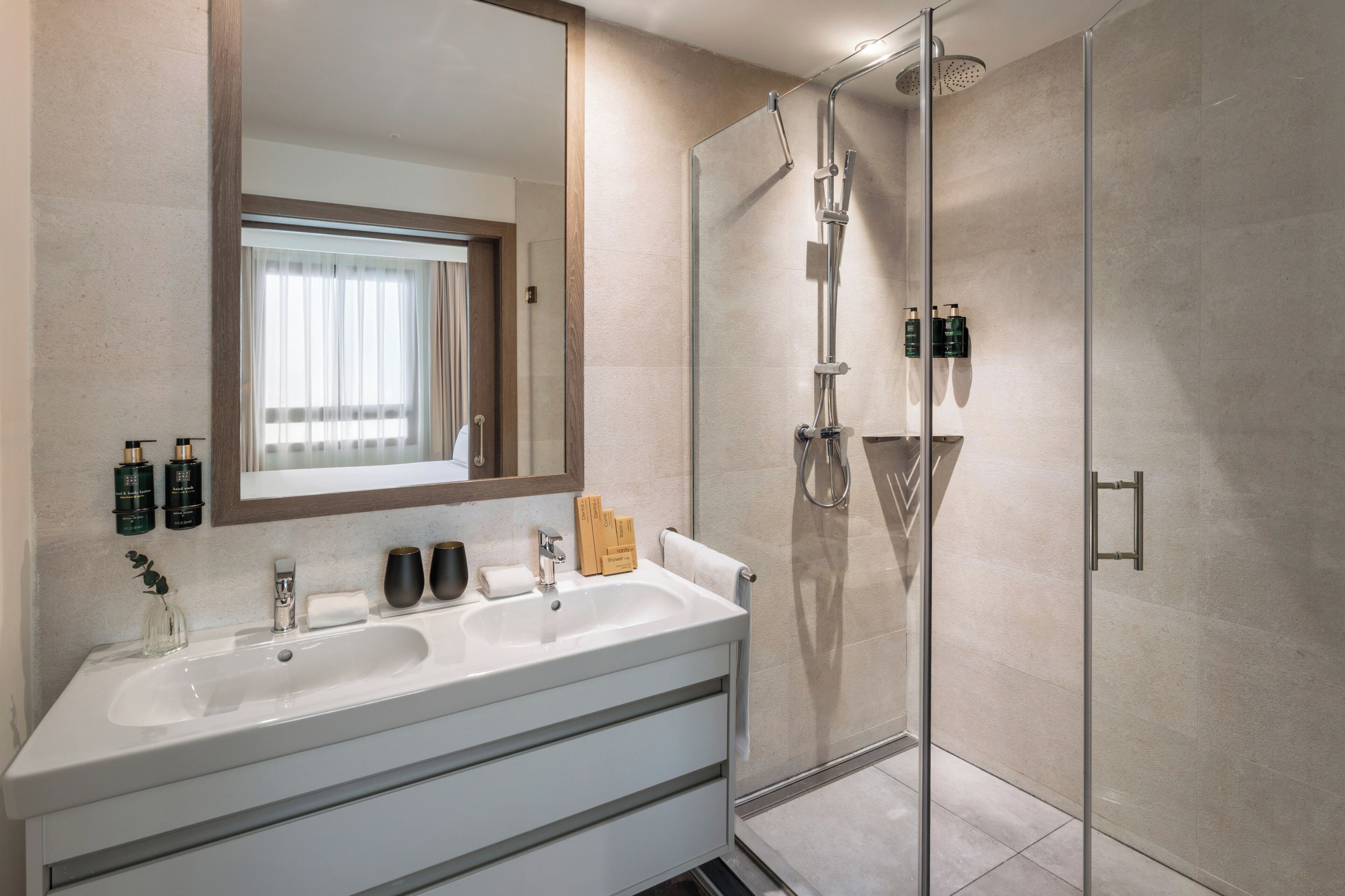 Un baño moderno con un espejo grande, un lavamanos y una ducha con cerramiento de vidrio.
