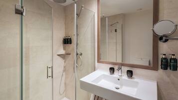 Een moderne badkamer met een douche met glazen wand, een witte wastafel en een grote spiegel.