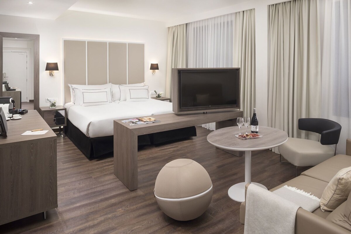 A hotel room with a bed, TV, desk, round table, and seating area.